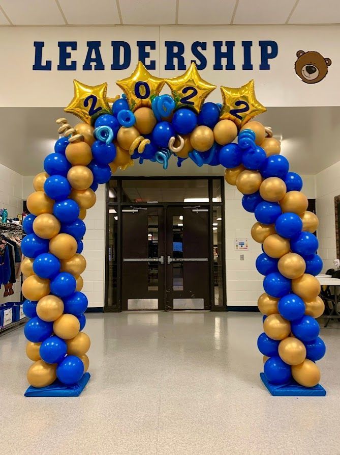 Blue and gold balloon arch with "2022" stars, in front of a door. The word "LEADERSHIP" is above it.