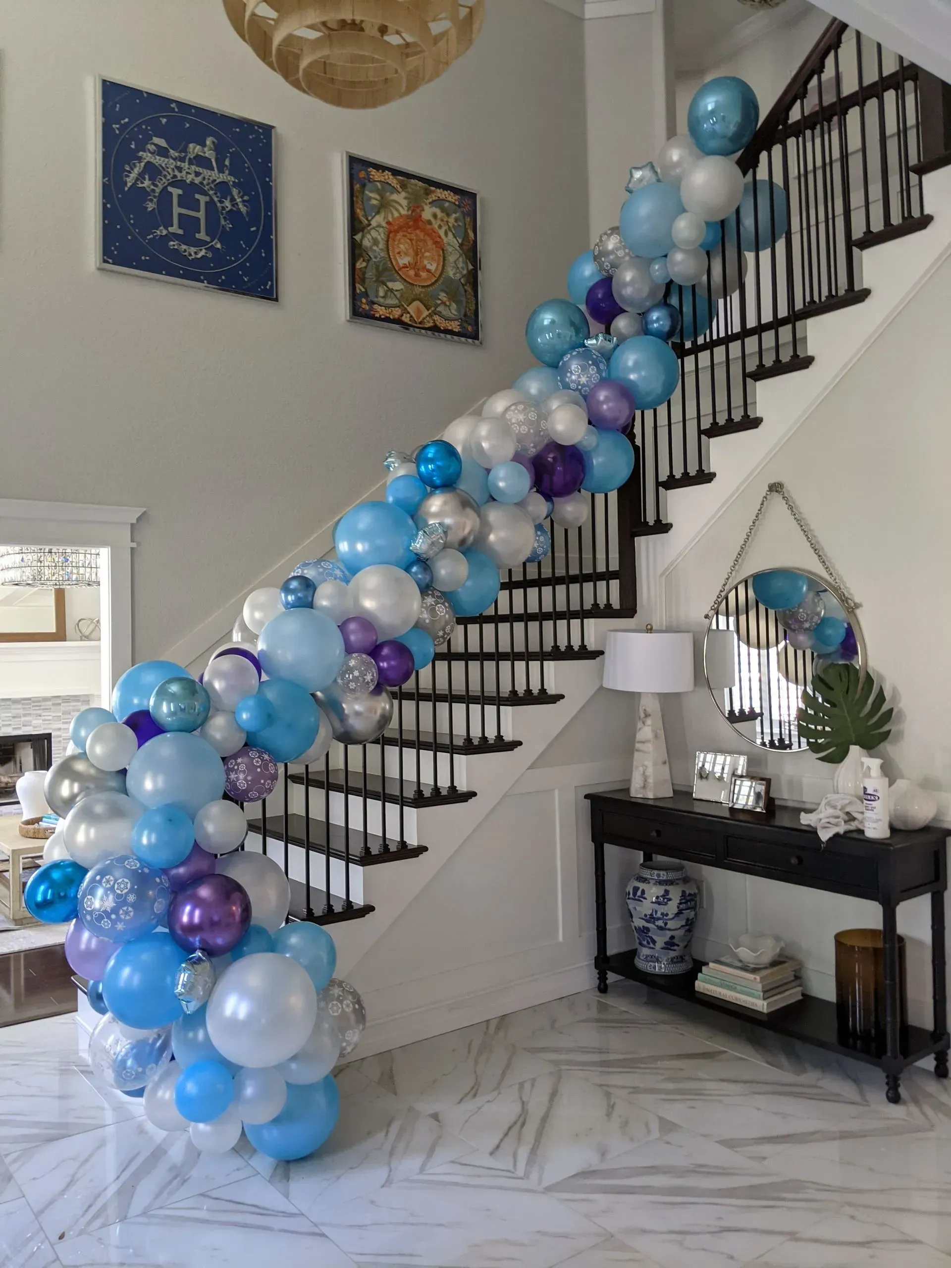 Balloon arch in shades of blue, silver, and purple cascading down stairs, decorated entryway.