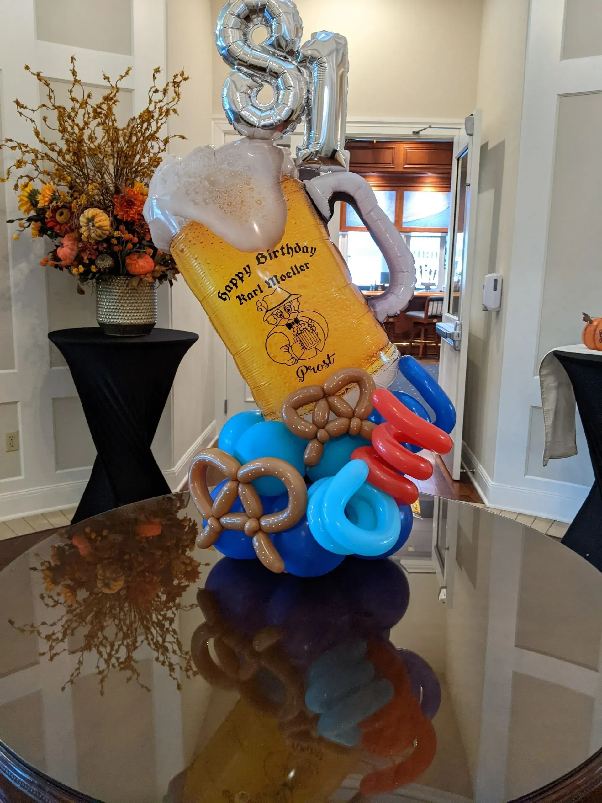 Balloon sculpture of a beer stein with "81" balloon above it. Pretzels and sausages at the base.