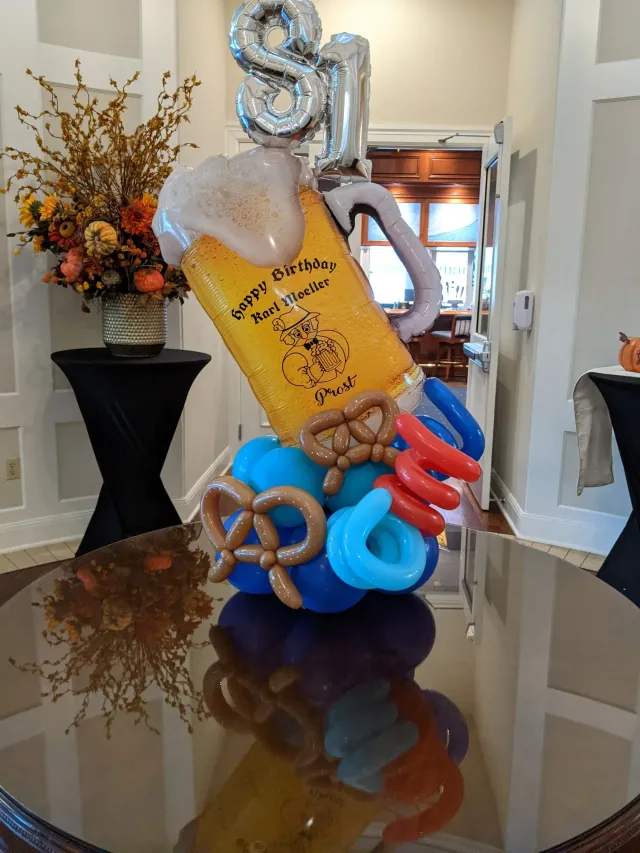 Balloon sculpture of a beer stein with "81" balloon above it. Pretzels and sausages at the base.