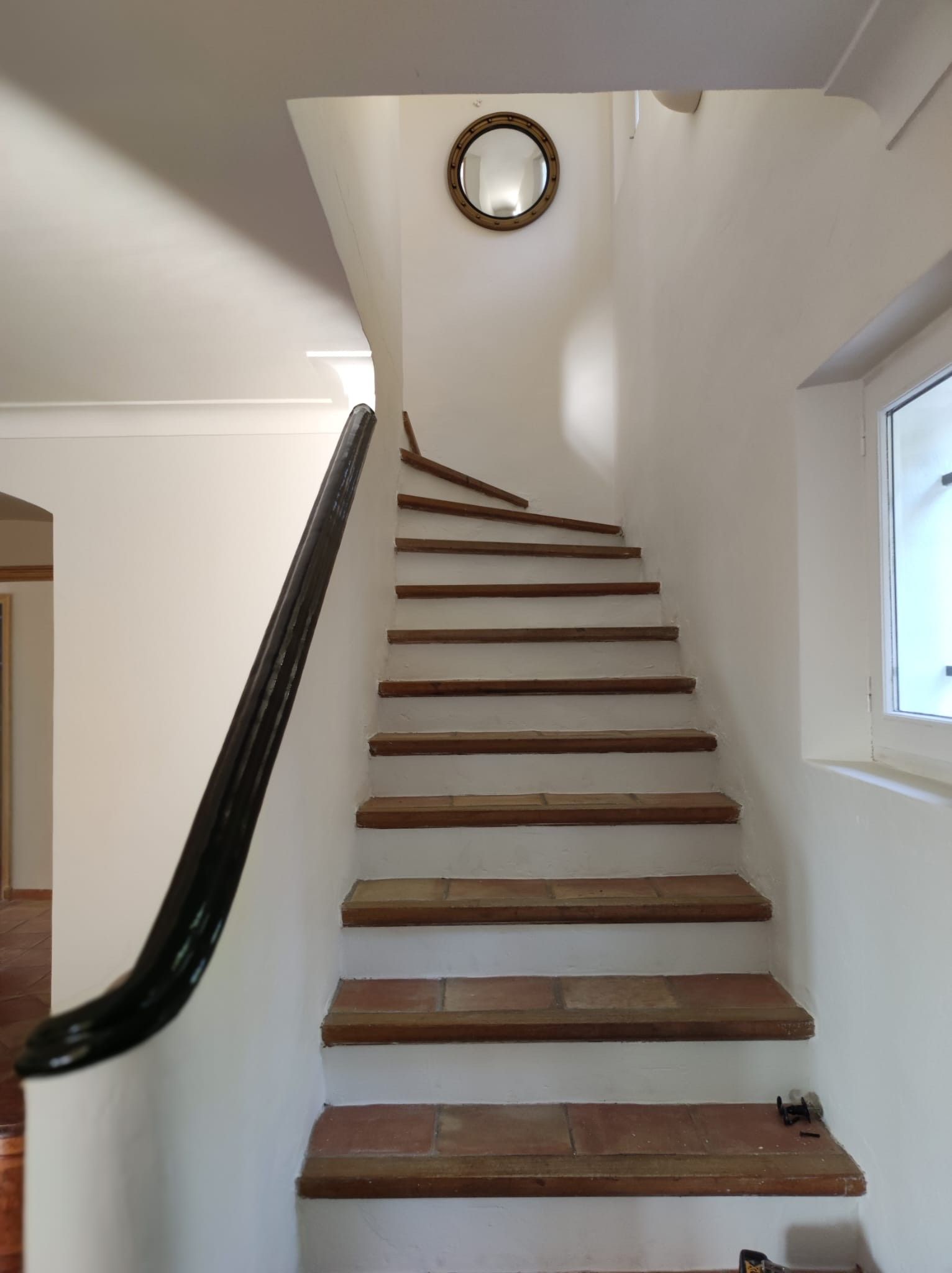 Een witte trap met houten treden en een zwarte leuning