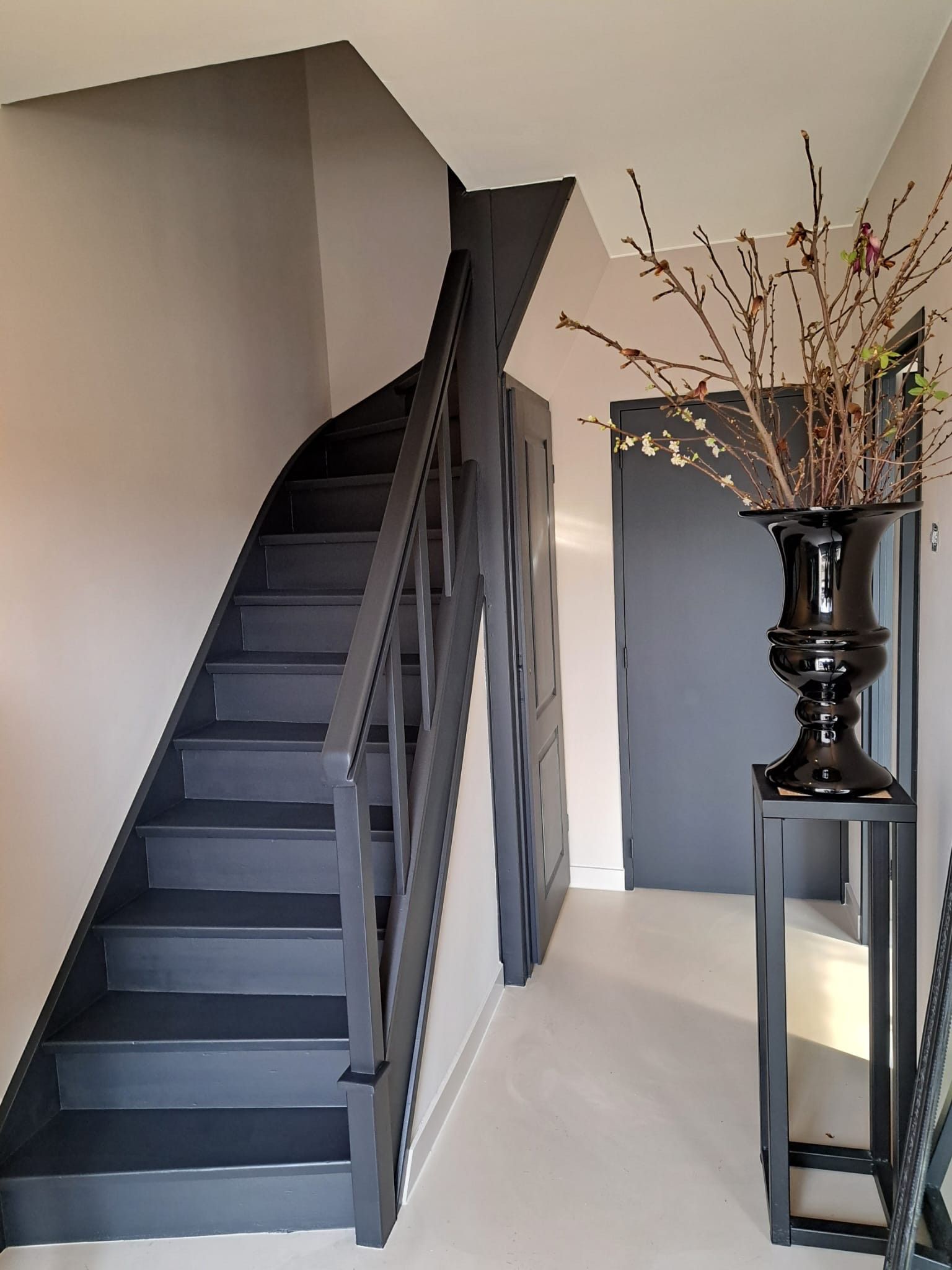Een zwarte trap in een gang met een vaas met bloemen op een tafel.