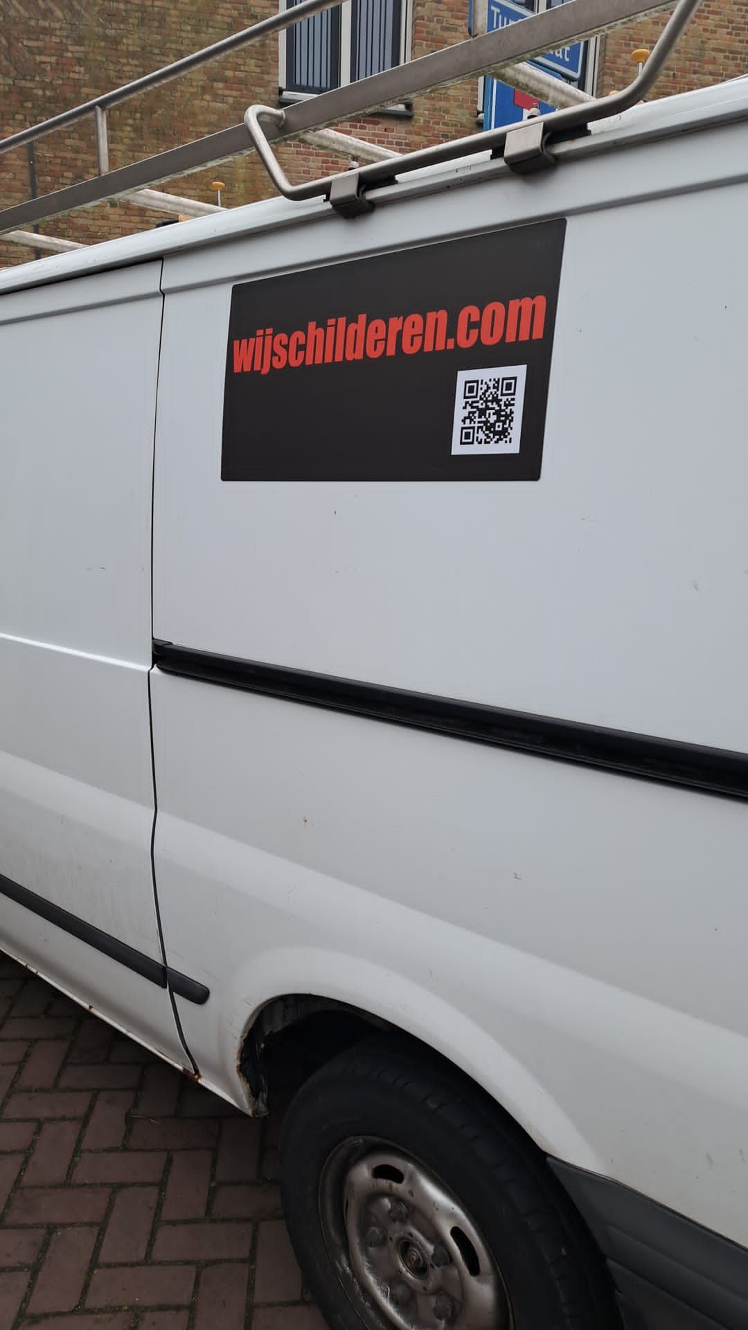 Een wit busje met een sticker op de zijkant met de tekst misschilderen.com