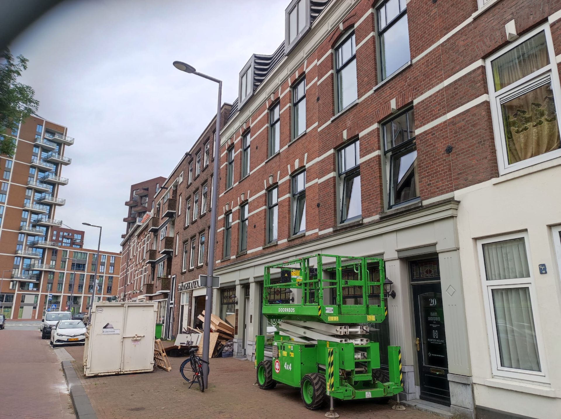 Voor een bakstenen gebouw staat een groene hoogwerker geparkeerd.
