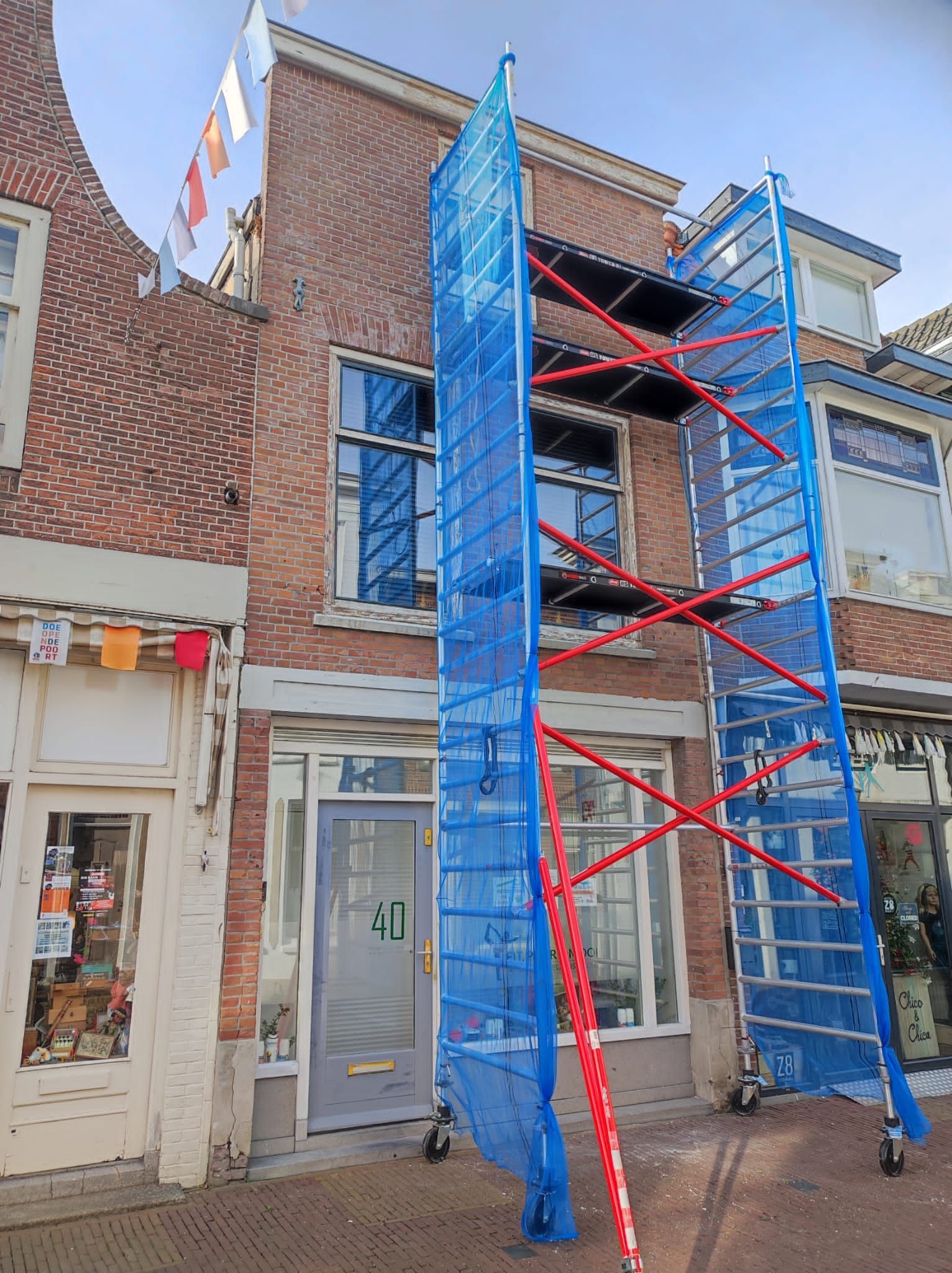 Voor een bakstenen gebouw staat een blauwe steiger.