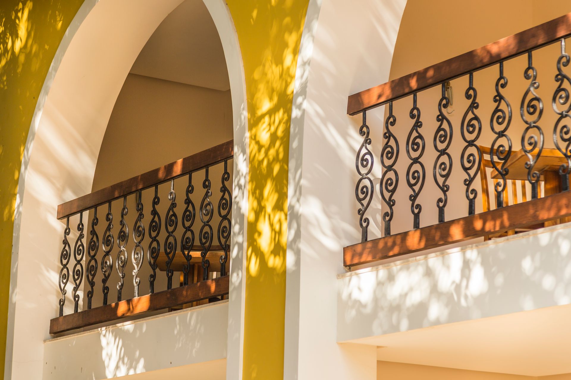 Uma varanda com uma grade de ferro forjado e uma parede amarela.