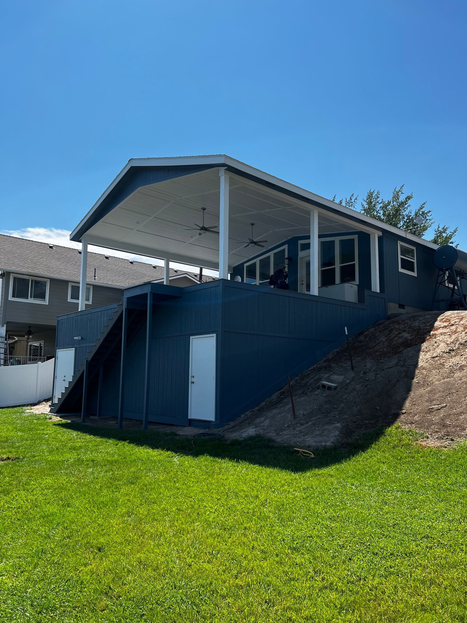 A house with a covered porch and stairs is sitting on top of a grassy hill.