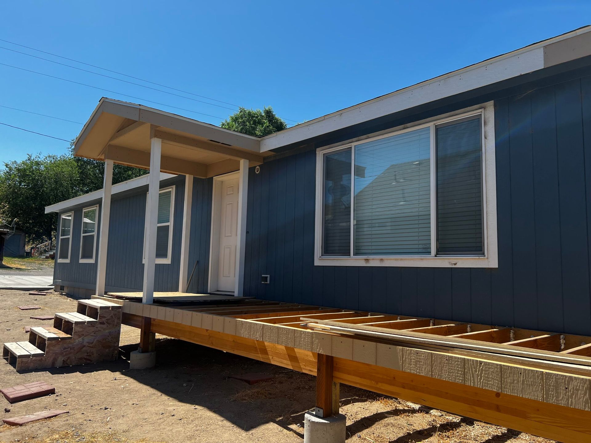 A blue mobile home with a wooden deck underneath it