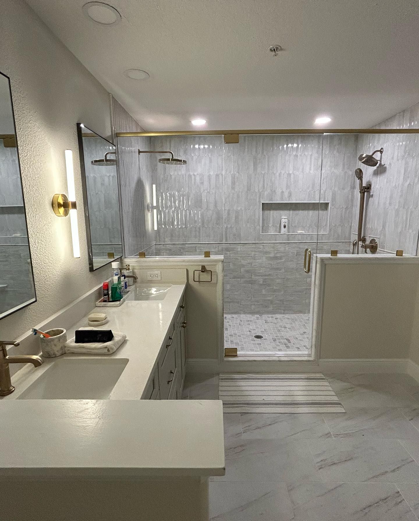 Modern bathroom with gold fixtures, white countertops, and large shower.