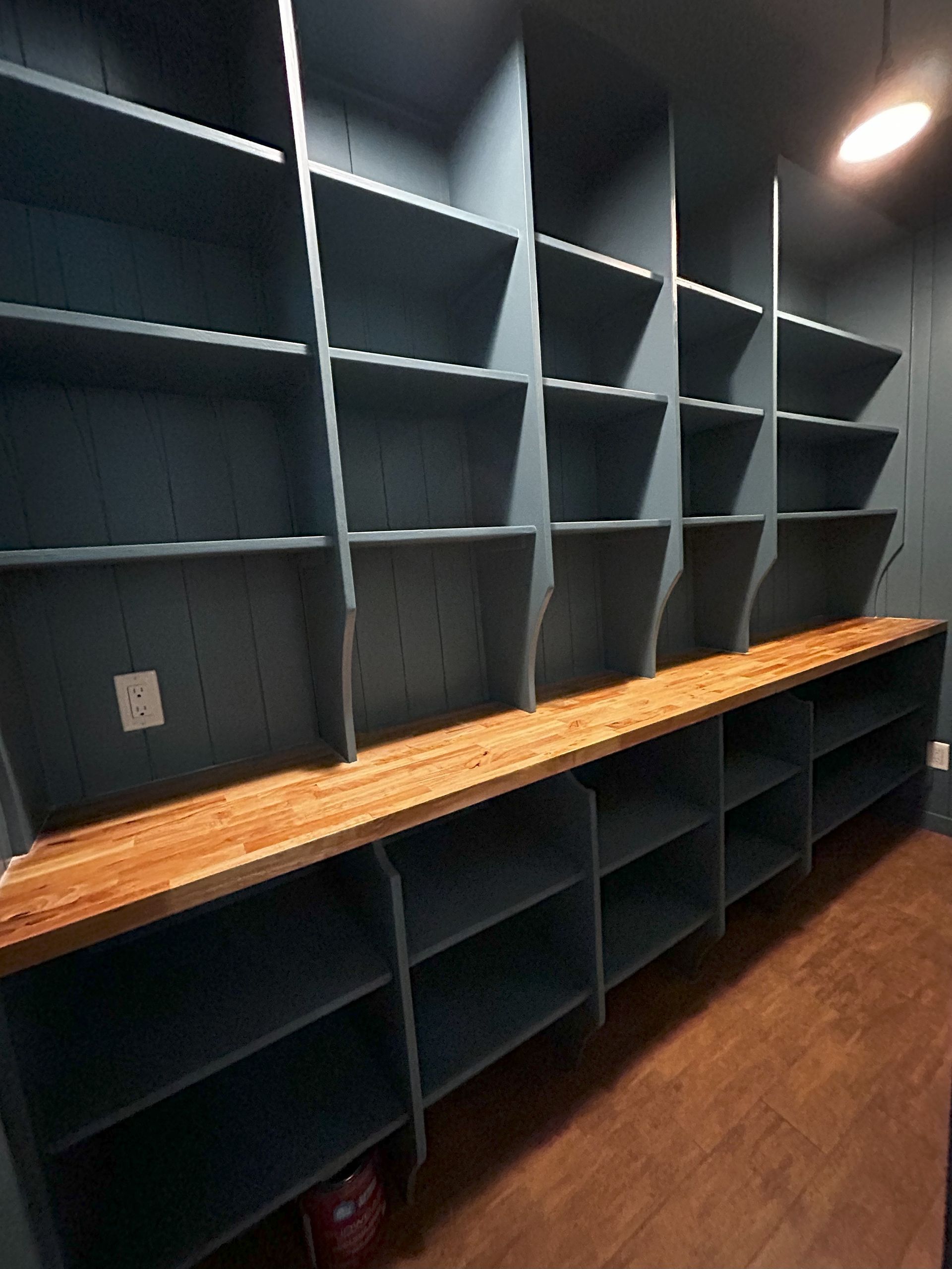Built-in blue pantry shelves with a wooden countertop, a power outlet, and brown flooring.