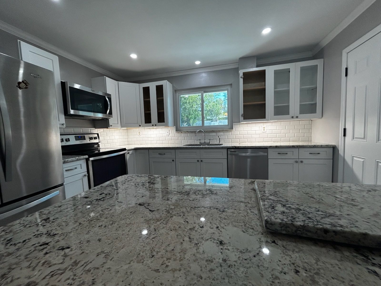 Kitchen with gray cabinets, granite countertops, stainless steel appliances, and a bright window.