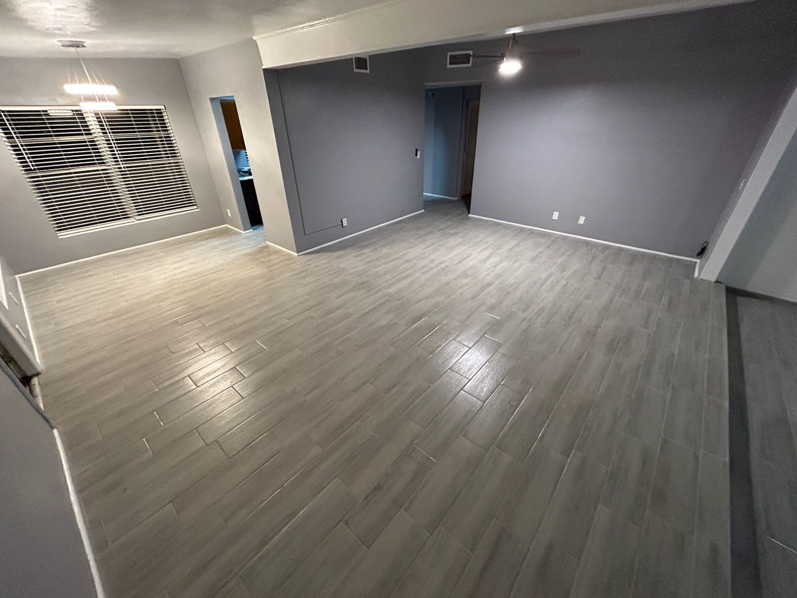 Empty living room with gray wood-look tile floor and gray walls. Natural light streams in from the window.