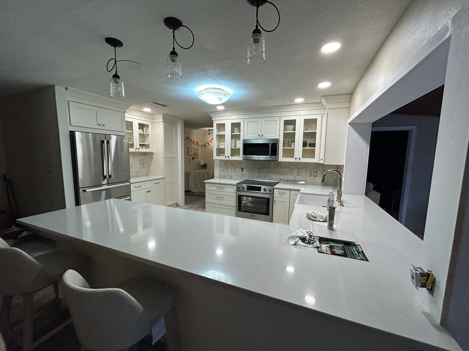 Modern kitchen with white cabinets, stainless steel appliances, and a large white countertop.