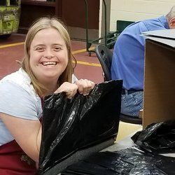A woman is smiling while holding a black plastic bag.