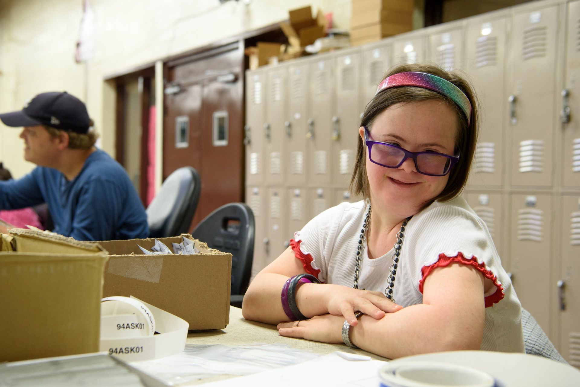 A young girl with down syndrome is sitting at a table with her arms crossed.