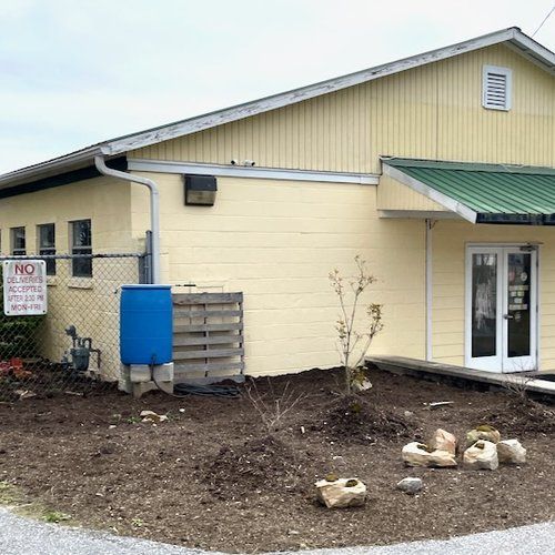 A yellow building with a green roof and a blue barrel in front of it.