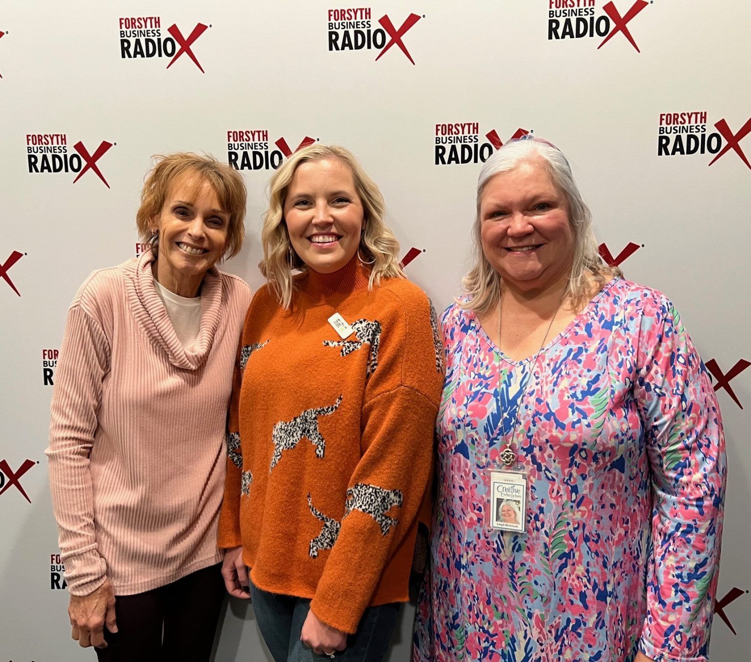 Three women are posing for a picture in front of a wall that says radio x.