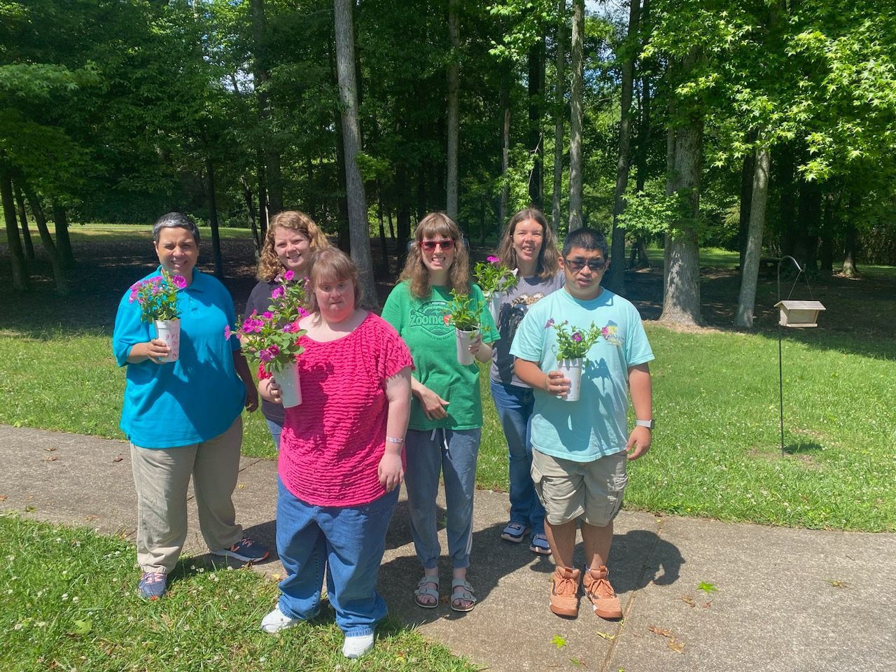 A group of people are standing in a park holding potted plants.