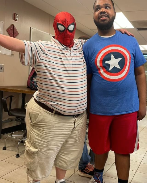 Two men are posing for a picture one is wearing a spider man mask and the other is wearing a captain america shirt