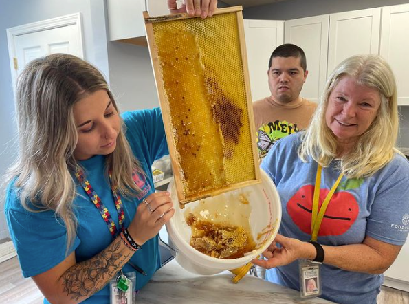 Two women are holding a honeycomb and a bowl of honey.