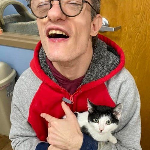 A man wearing glasses is holding a black and white kitten in his arms.