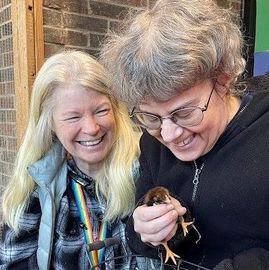 Two women are holding a small bird in their hands and smiling.