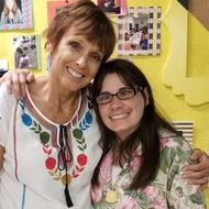 Two women are posing for a picture in front of a yellow wall.