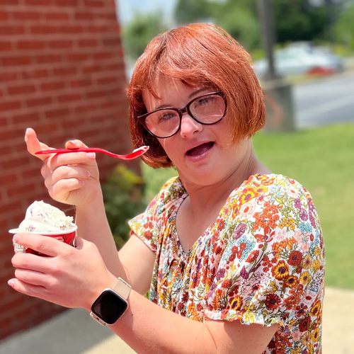 A woman wearing glasses is eating ice cream with a spoon.
