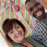 A man and a woman are smiling in front of a christmas present.