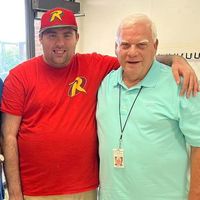 Two men are posing for a picture together and one of them is wearing a robin hat.