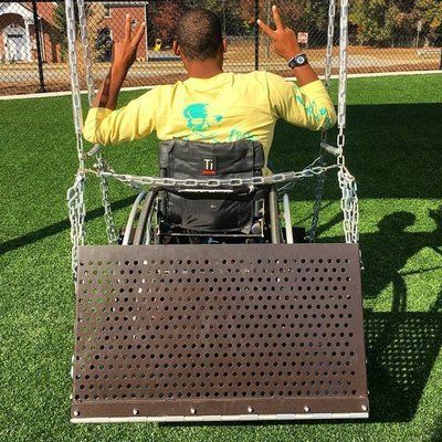 A man in a wheelchair is sitting on a swing and giving a peace sign.