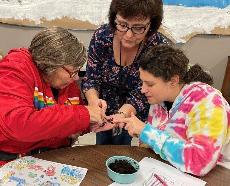 Three women are sitting at a table looking at a bug.