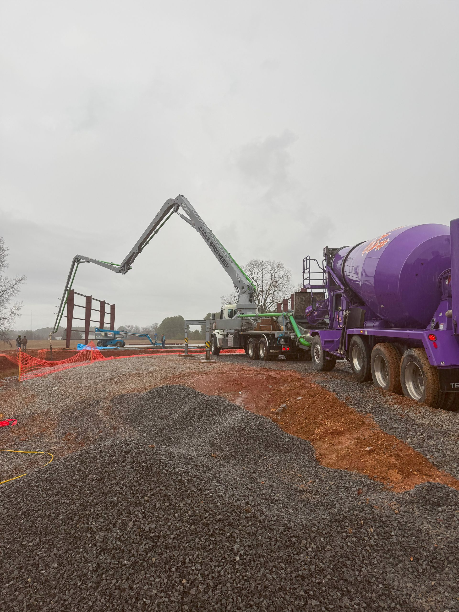 A purple concrete mixer truck is pouring concrete on a gravel road.