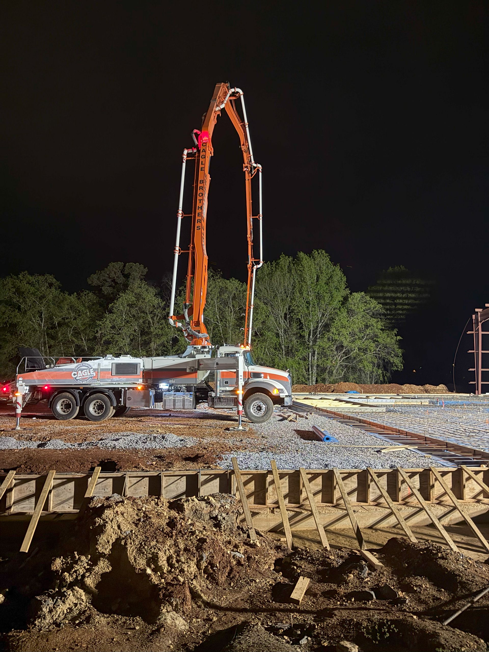 A concrete pump is pumping concrete into a construction site at night.