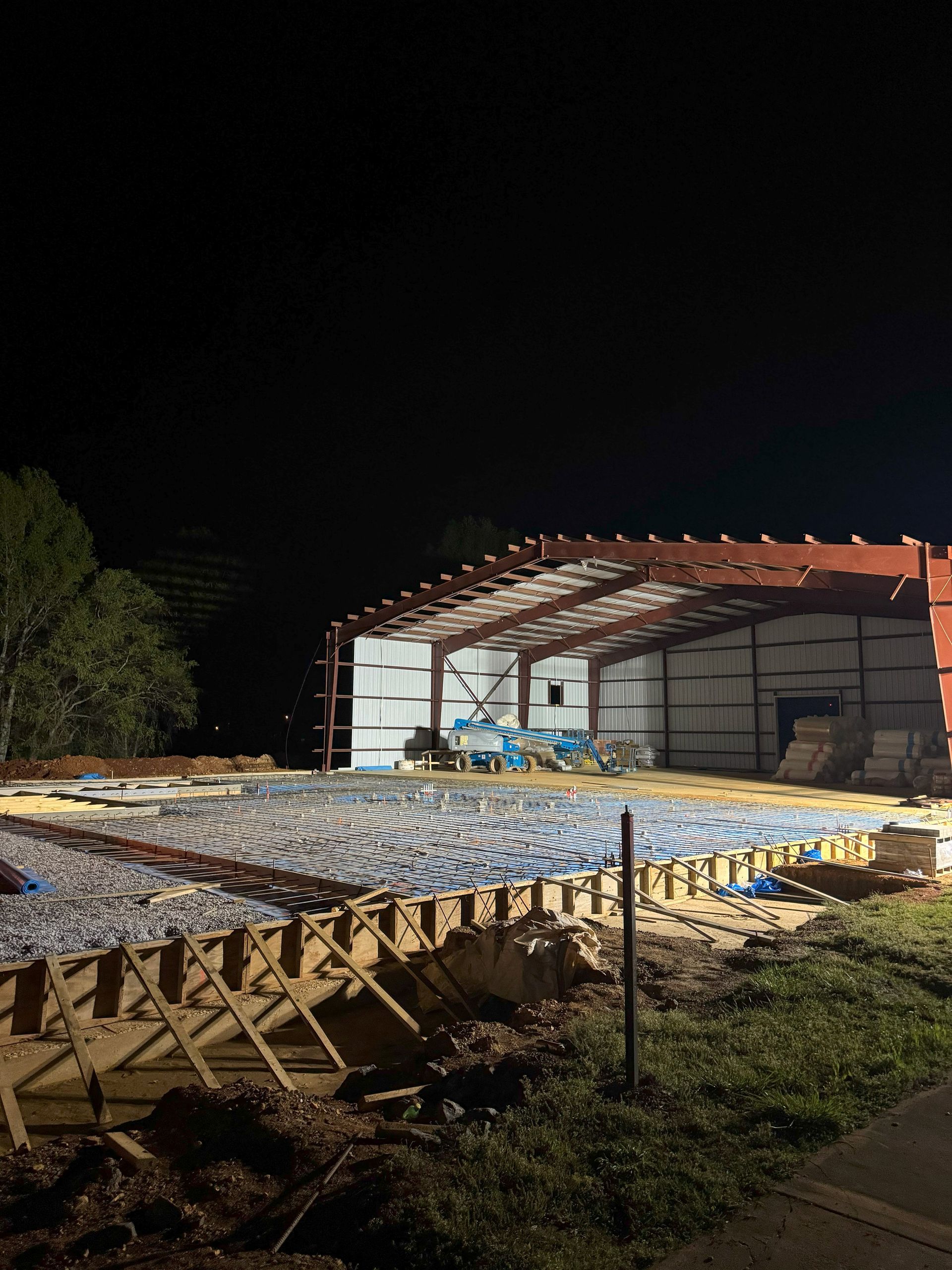A large building is being built at night with a lot of concrete on the ground.