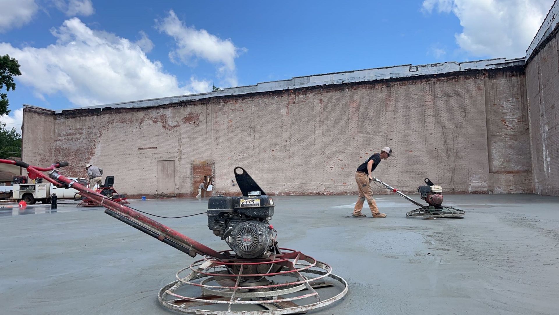 Two men are working on a concrete floor in front of a large building.