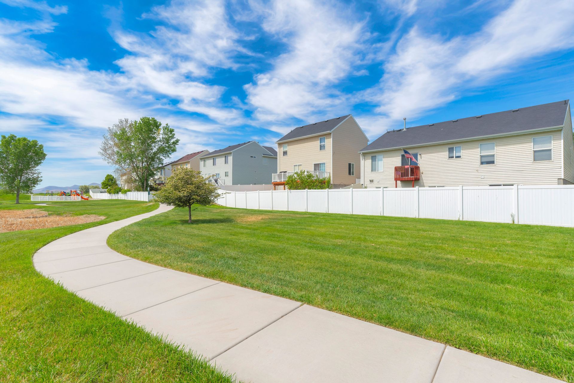 A concrete walkway leading to a row of houses with a white fence.