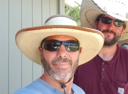 Two people wearing sun hats and sunglasses pose for a selfie outdoors.