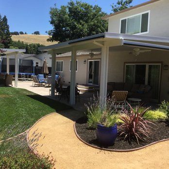 A backyard patio with a covered porch, outdoor furniture, a curved gravel path, and landscaping under a clear blue sky.