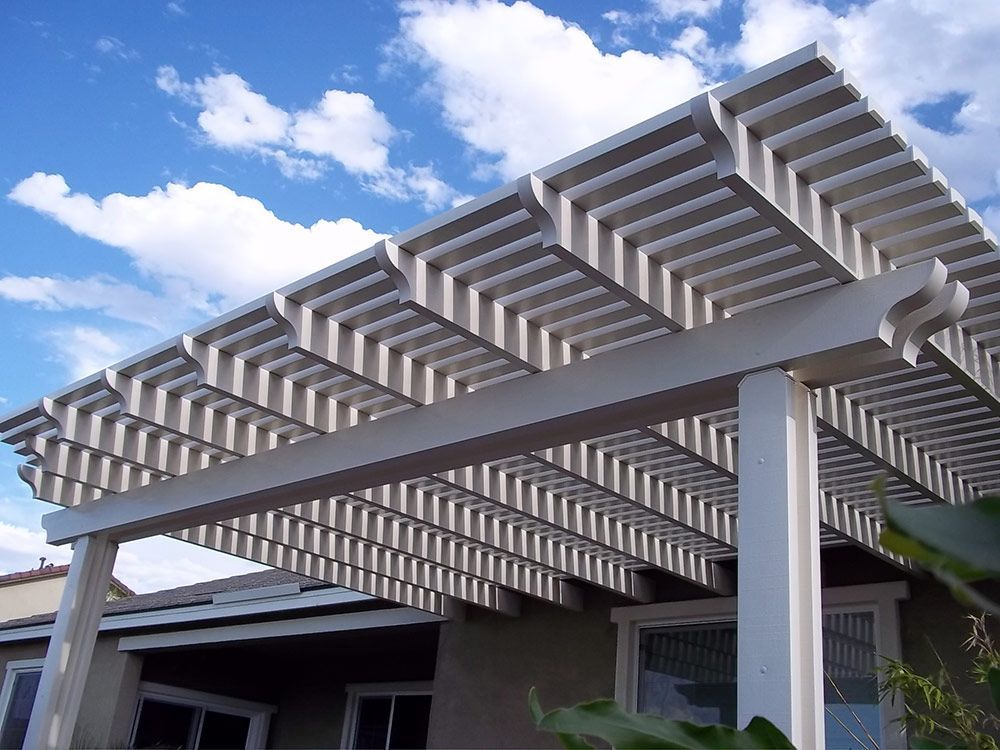 A white lattice pergola extends from the side of a house against a bright blue sky with white clouds.