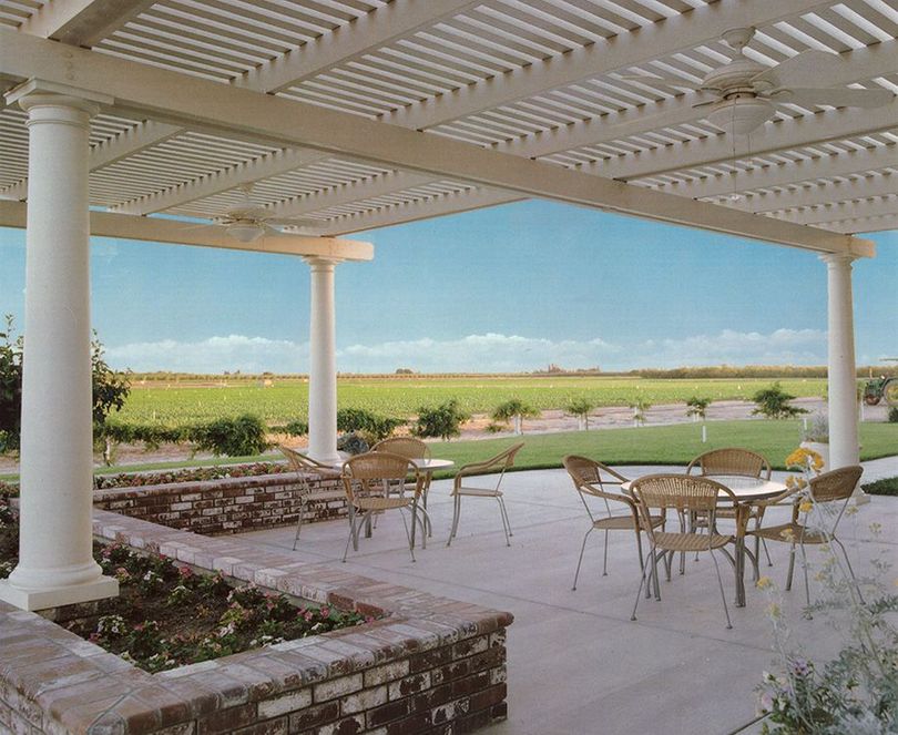 A patio with a white lattice pergola, circular columns, brick planter boxes, and a dining set overlooking a vineyard.