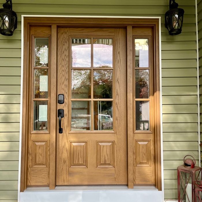 Wooden front door with glass panes, flanked by sidelights, set in green siding.