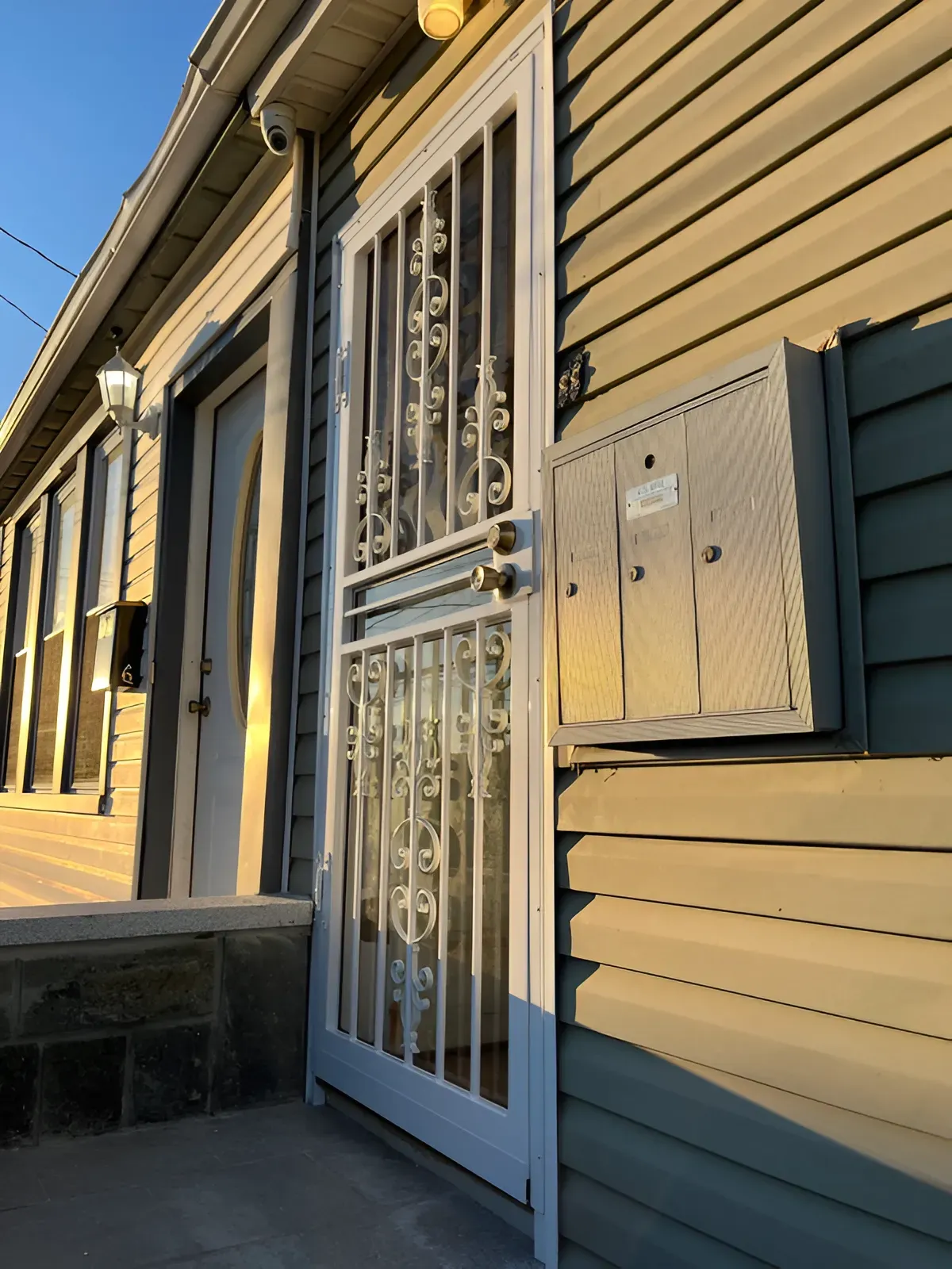 A front door with a security gate, mailbox, and siding on an older building.