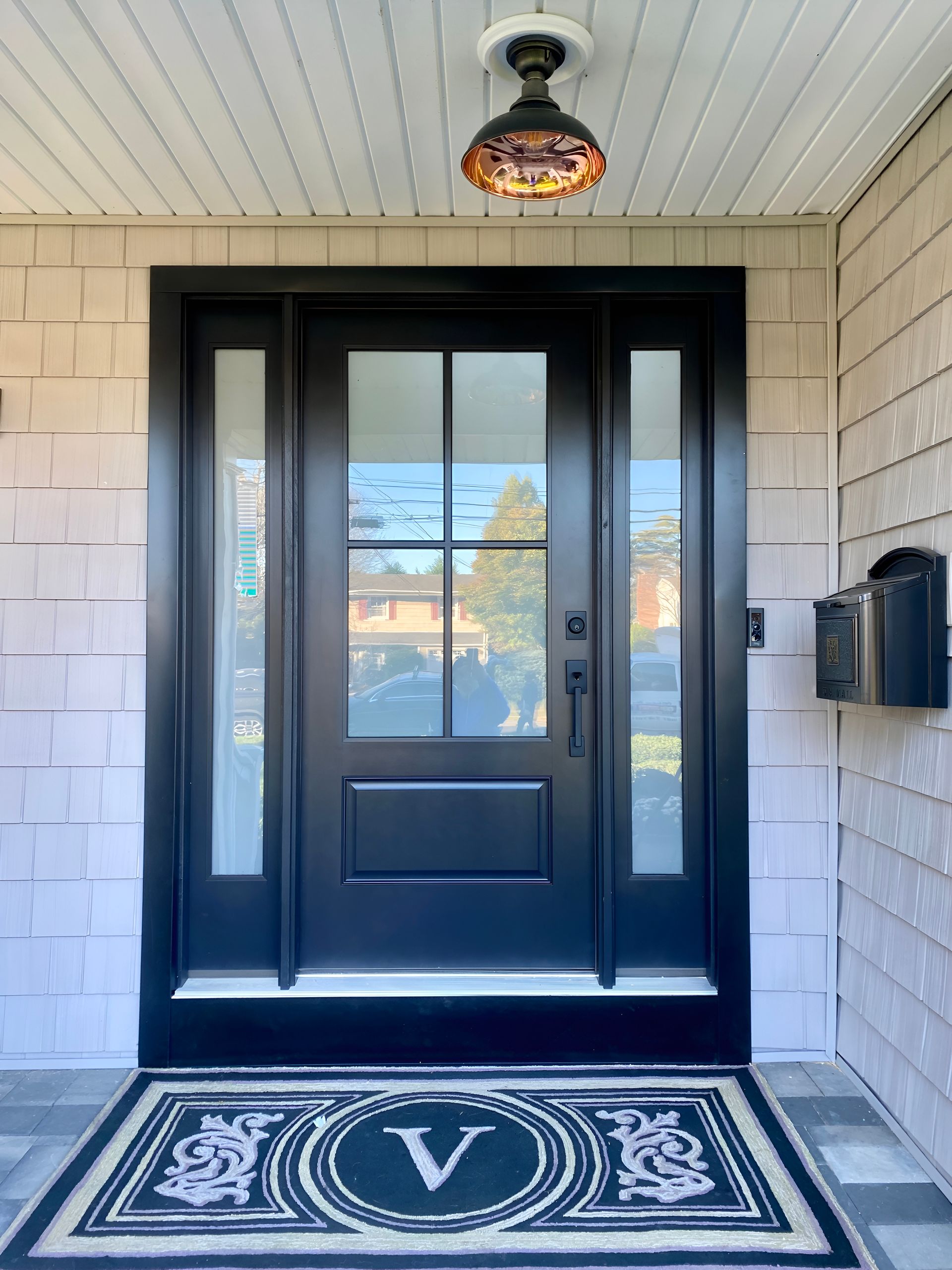 Black front door with sidelights and a transom, welcome mat with the letter 