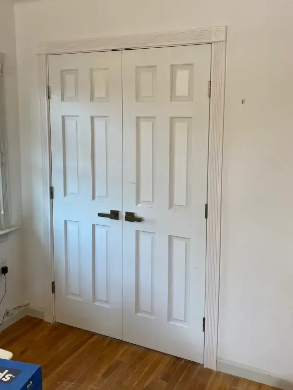 White double doors with black handles in a room with wood floors and white walls.
