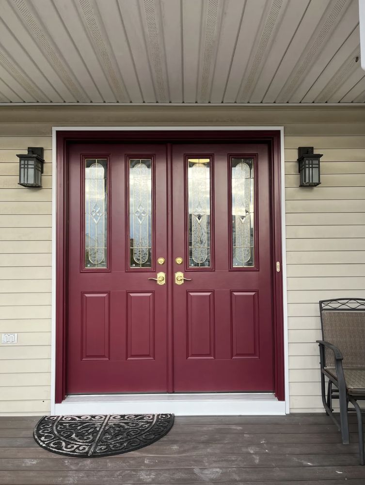 Double burgundy front doors with glass panels, flanked by black sconces.