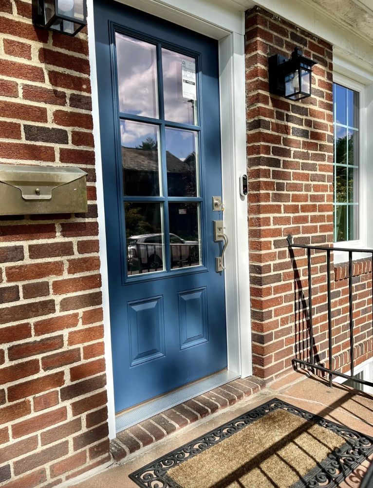 Blue front door with glass panes and brass hardware on a brick house with a porch.