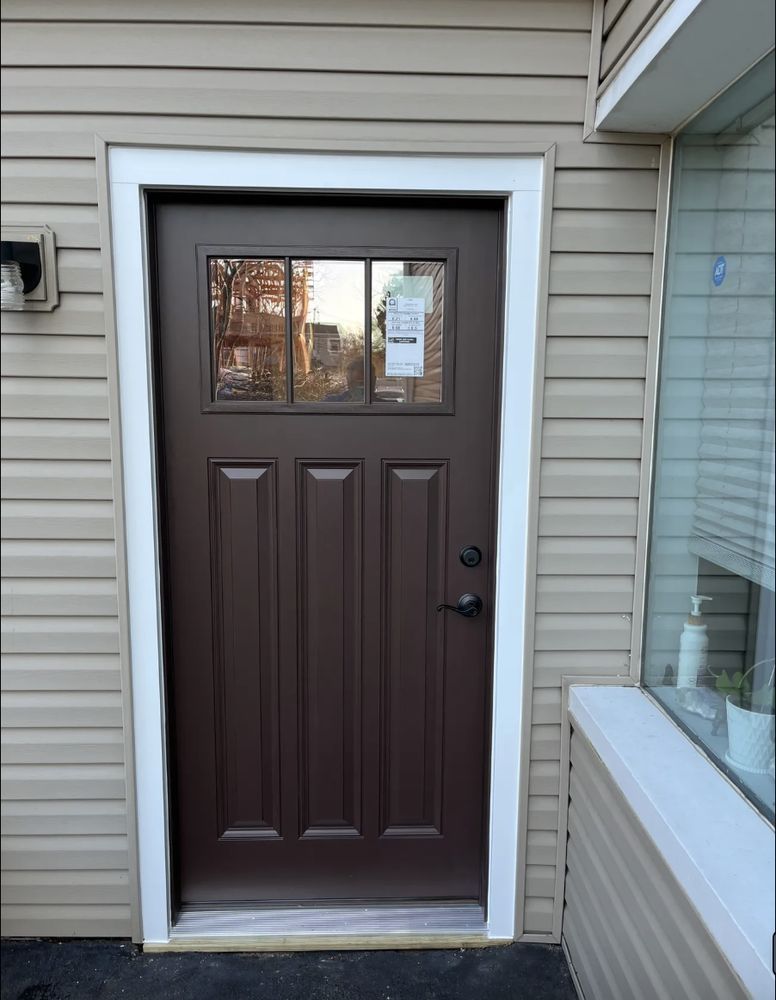 Brown door with glass pane, white trim, on a tan house with a window to the right.