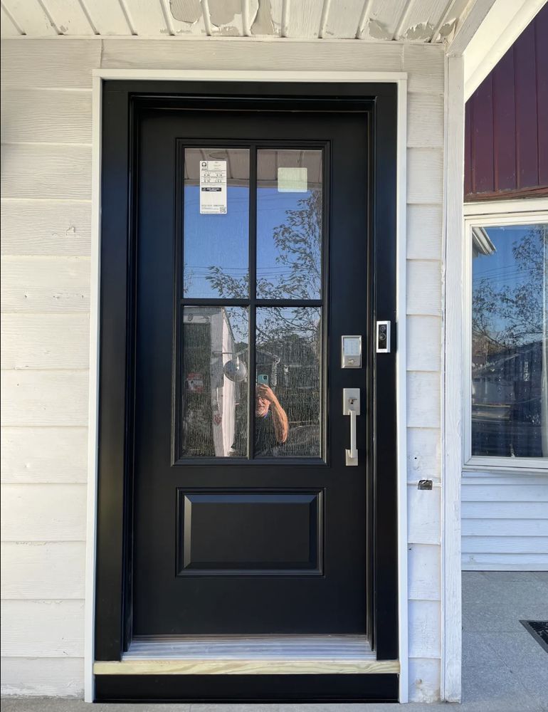 Black front door with glass panes, silver hardware, set in white frame, against white siding.