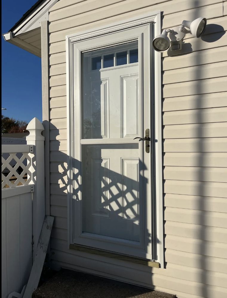 White door with screen and security lights on a siding house next to a white lattice fence.